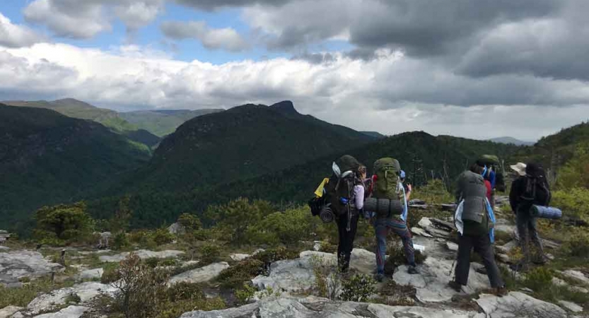 A group of backpackers hike along a rocky trail overlooking a mountainous landscape